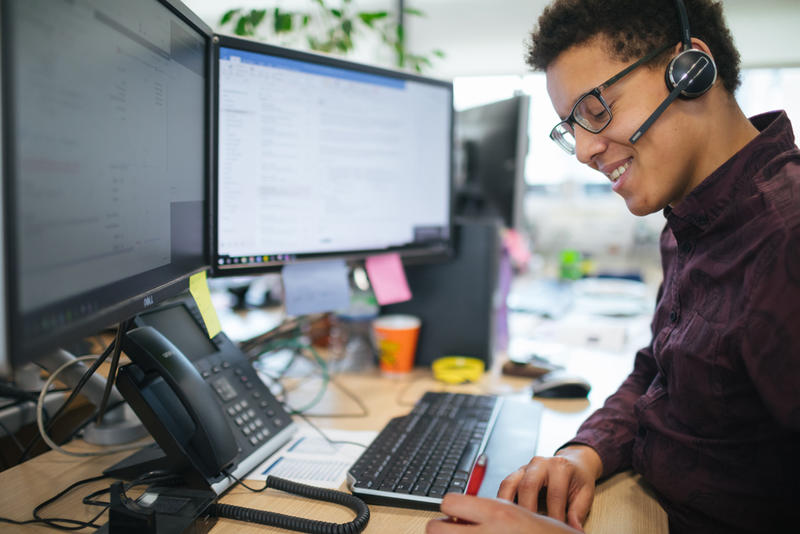 Smiling man with headset and two computer monitors