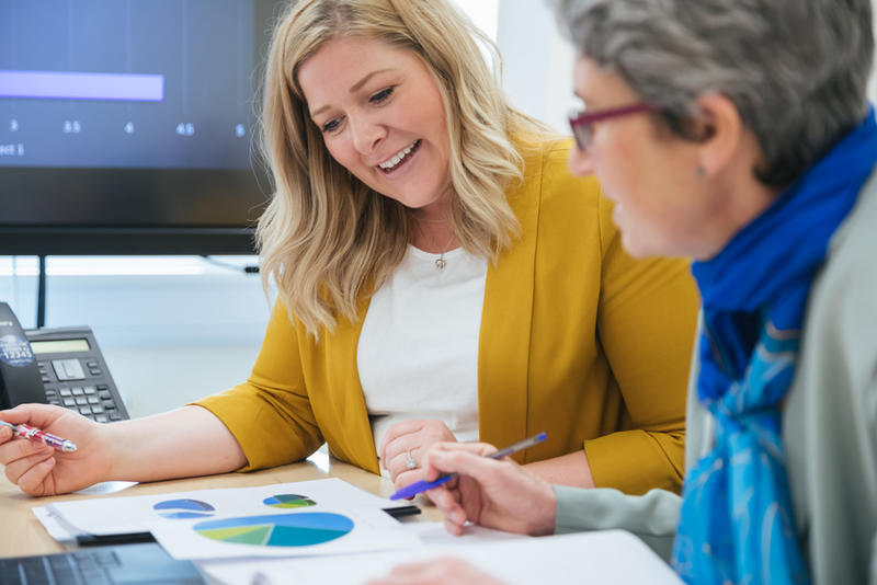 Two women at a desk looking at papers with pie charts on.